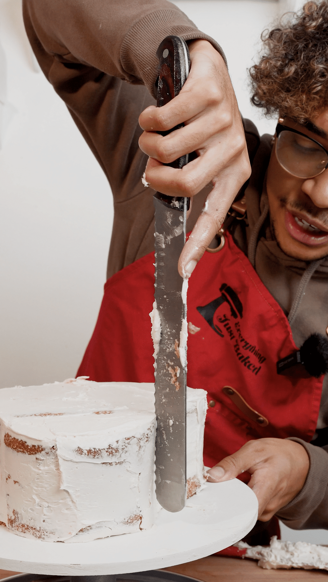 Baker using a serrated knife to cut a small wedge from the top center of a cake to enhance the heart shape.